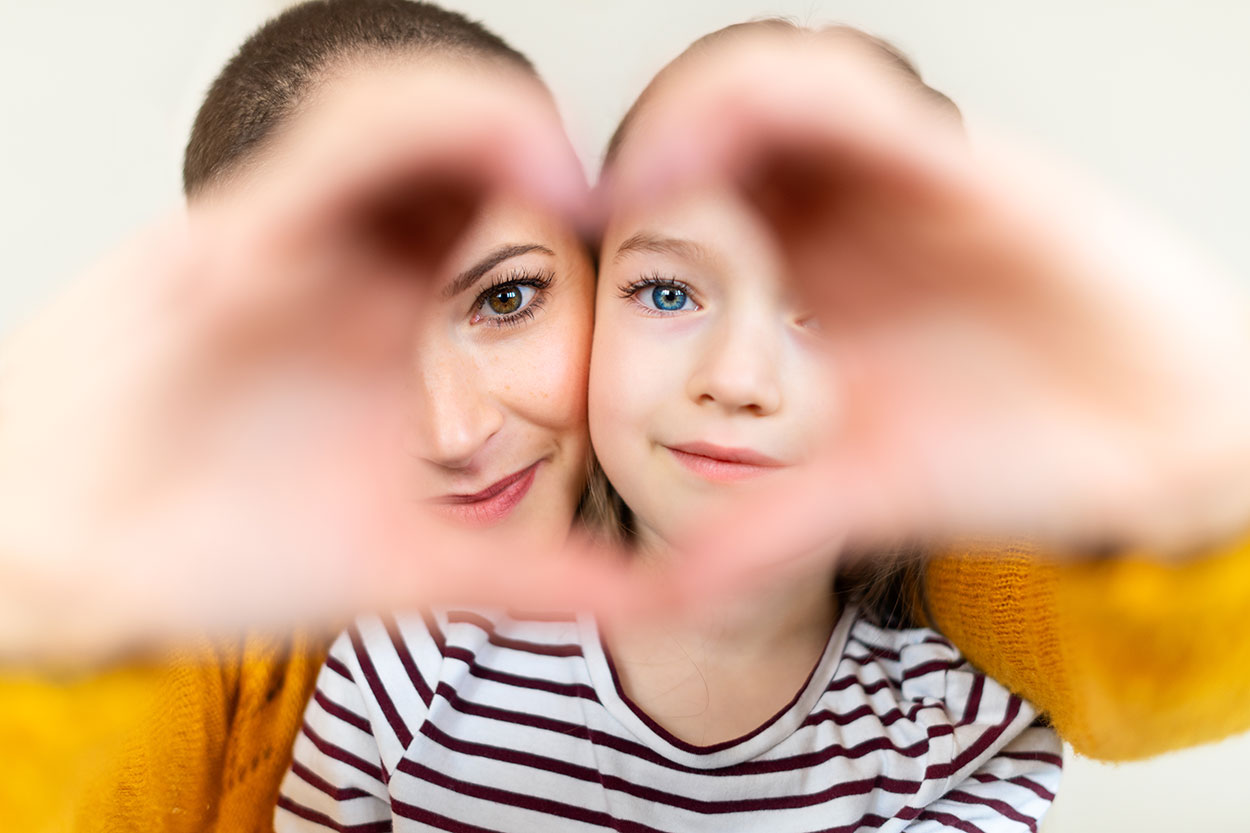 A mother and daughter making a heart symbol with their hands